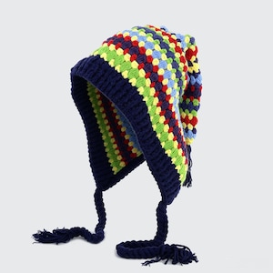 May include: A crochet beanie with earflaps featuring a multi-colored pattern of red, yellow, light blue, and lime green yarn. The hat has a solid dark navy blue ribbed border and two long, braided dark navy blue ties with tassels at the ends.
