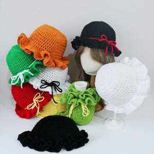 May include: A collection of handmade crochet hats in various colors, including orange, green, white, red, yellow, and black. Each hat features a ruffled brim and some have decorative bows. A green drawstring bag is also visible.