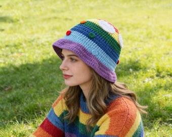 Sombrero tipo cubo de ganchillo hecho a mano con diseño de arcoíris y apliques de nubes y puntos.