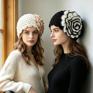 May include: Two crochet beanies, one cream-coloured with a matching side flower and one black with a large white and black layered flower. Both hats feature a textured, scalloped knit pattern and are worn to showcase the floral embellishments.