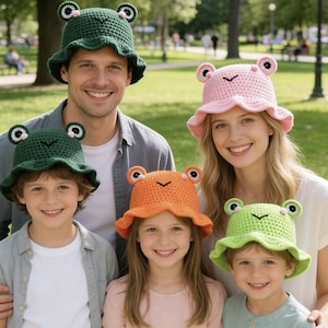May include: A collection of five crochet bucket hats featuring frog designs with protruding eyes and pink cheeks. The hats are available in dark green, light green, orange, and pink, each crafted with a wide brim and a textured knit pattern.