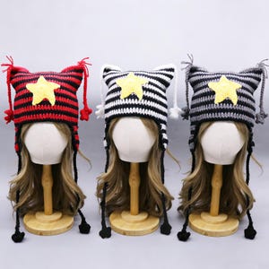 May include: Three handmade crochet hats with star accents. The hats feature striped patterns in red and black, black and white, and gray and black. Each hat has a yellow star and dangling tassels.