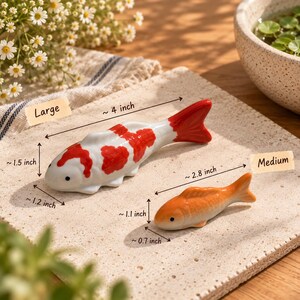 May include: Two ceramic fish-shaped chopstick rests. The large white fish has red spots and measures approximately 4 inches long, 1.5 inches high, and 1.2 inches wide. The medium orange fish measures approximately 2.8 inches long, 1.1 inches high, and 0.7 inches wide.