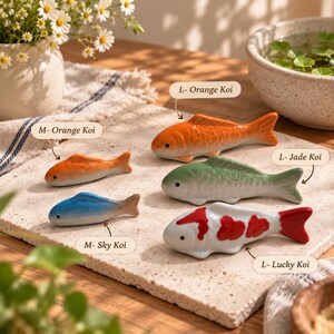 May include: A collection of ceramic fish-shaped chopstick rests in various sizes and colors. The set includes an orange koi, a jade koi, a lucky koi with red spots, a smaller orange koi, and a blue sky koi, each labeled with its specific name.