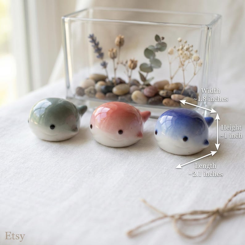 May include: Three small, smooth, whale-shaped ceramic figurines in sage green, soft pink, and gradient blue. Each figurine features two black dot eyes and measures approximately 1.8 inches wide, 1 inch high, and 2.1 inches in length.