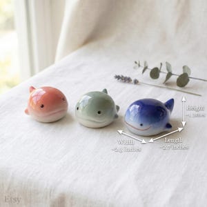 May include: Three small ceramic whale figurines in pink, light green, and blue. Each whale has a smooth, glossy finish and simple black eyes. Dimensions are approximately 1.3 inches in height, 2.3 inches in width, and 2.7 inches in length.