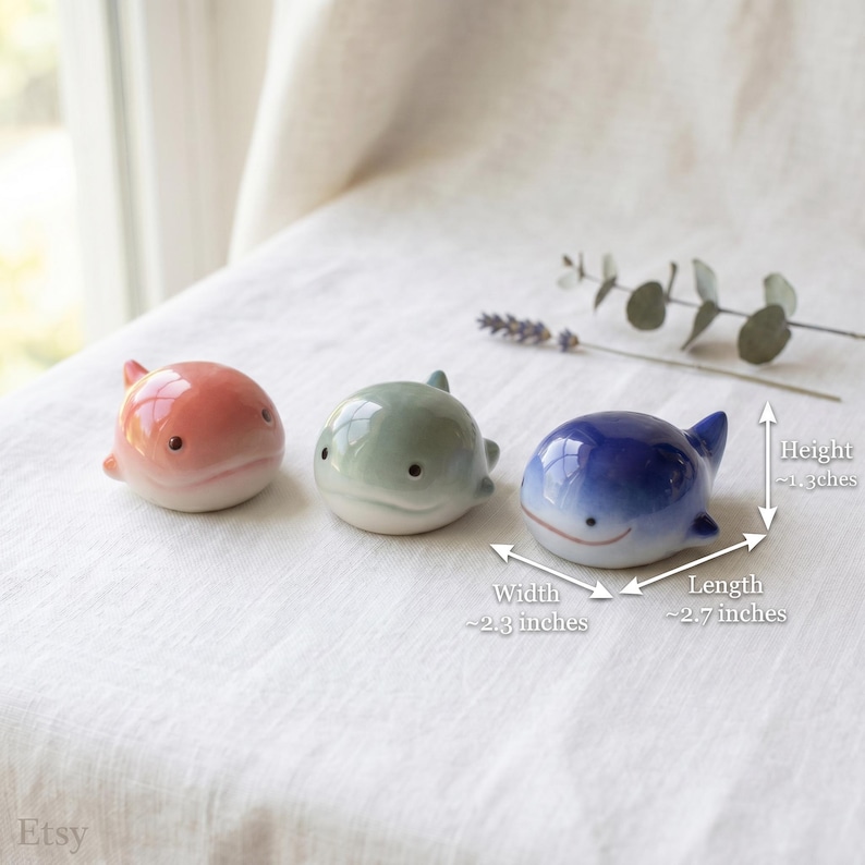 May include: Three small ceramic whale figurines in pink, light green, and blue. Each whale has a smooth, glossy finish and simple black eyes. Dimensions are approximately 1.3 inches in height, 2.3 inches in width, and 2.7 inches in length.