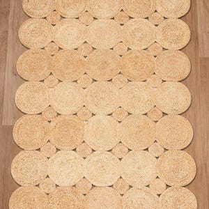 May include: A natural fiber rug with a repeating pattern of connected circles. The rug is made of a light tan material and has a textured surface. The circles are arranged in rows and columns, creating a geometric design. The rug is suitable for indoor use.