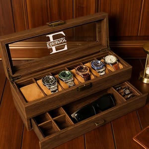 May include: A wooden watch box with a glass top, displaying six wristwatches on tan cushions. The box has a lower drawer with compartments for accessories and a pair of sunglasses. The box is brown with a white monogram.