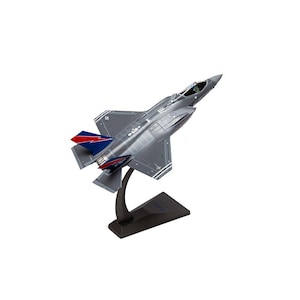 May include: A detailed model of a gray F-35 fighter jet, mounted on a black display stand. The jet features red and blue accents on the tail fins and wings. The model is angled upwards, showcasing its design.