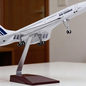 Può includere: Un modello bianco dell'aereo supersonico Concorde Air France. Il modello presenta il logo Air France e i colori della bandiera francese sulla coda. È montato su un supporto argentato con una base marrone.