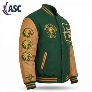 May include: A dark green varsity jacket with tan leather sleeves. The chest features a circular Liberty Academy Eagles logo. The right sleeve displays three eagle head patches and the text State Champions 2023. A large letter E is on the chest.