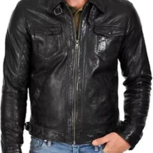 May include: Black leather jacket with a collared neckline, two chest pockets, and a zip-up front. The jacket has a classic design and is worn with blue jeans. The jacket has a buckle detail at the waist.