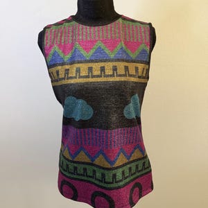 May include: A sleeveless top with a black background and a colorful geometric pattern. The design includes pink, green, blue, and gold shapes, with cloud-like accents. The top is displayed on a black mannequin.