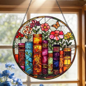 May include: A round stained glass window hanging featuring colorful flowers and books. The design includes red, pink, and yellow flowers, with a butterfly. The books are in various colors and patterns. The window is suspended by a chain.