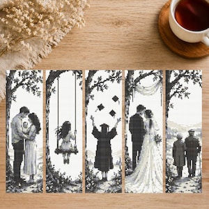 Pode incluir: Um conjunto de cinco painéis de ponto cruz em preto e branco retratando eventos da vida. As cenas incluem um casal abraçado, uma menina num baloiço, uma formatura, um casamento e um casal de idosos a caminhar. Os painéis são exibidos numa superfície de madeira.