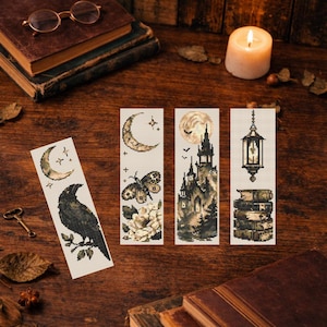 Puede incluir: Cuatro marcapáginas decorativos con diseños góticos bordados a punto de cruz. Presentan un cuervo, una luna creciente y estrellas, una mariposa y flores, un castillo bajo la luna llena y una linterna sobre libros. Sobre una superficie de madera.