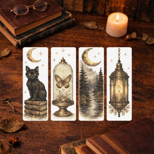 Peut inclure: Quatre marque-pages décoratifs sur le thème gothique. L'un représente un chat noir sur des livres, un autre un papillon dans un dôme en verre, un troisième une scène de forêt et le dernier une lanterne. Les marque-pages sont sur une surface en bois.