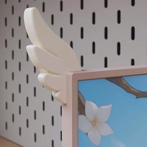 May include: A cream-coloured wing-shaped decorative element attached to the corner of a screen. The screen displays a floral design with a white flower against a blue sky. The background features a white pegboard with black slots.