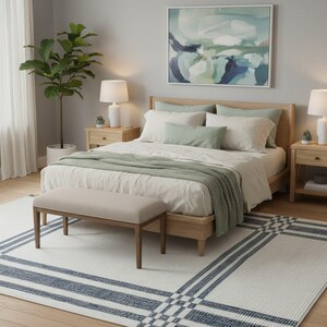 Peut inclure: Une chambre à coucher avec un lit en bois clair, une literie blanche, des coussins et une couverture verts. Un banc beige est au pied du lit. Un tapis blanc à rayures bleues et une grande peinture complètent la pièce.