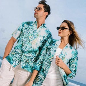 May include: A matching set of teal and white patterned shirts and jackets. The short-sleeved button-down shirt is paired with white shorts. The jacket has long sleeves and is worn over a white vest and white shorts. Both outfits feature a paisley design.
