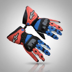 May include: A pair of motorcycle gloves in red, black, blue, and white. The gloves have a carbon fiber knuckle protector and a white logo on the cuff. The fingers are segmented for flexibility, with red and blue accents.