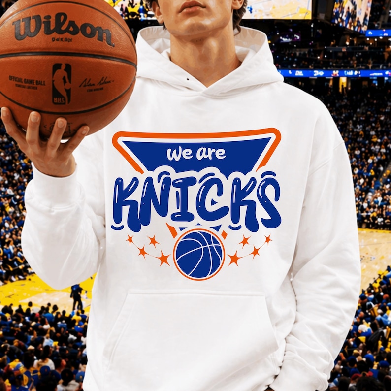 Pu&ograve; includere: Felpa con cappuccio bianca con la scritta "we are KNICKS" in blu e arancione, insieme a una grafica di basket. Nell'immagine &egrave; tenuto un pallone da basket marrone con il logo Wilson.