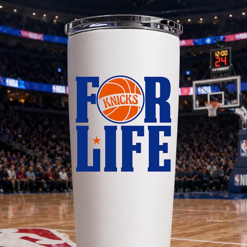 Pu&ograve; includere: Bicchiere bianco con bordo argentato. Il testo "FOR LIFE" &egrave; in blu, con "KNICKS" e una grafica di basket in arancione. Una stella arancione &egrave; sotto "FOR". Lo sfondo mostra un campo da basket e tribune.