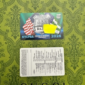 May include: Two cards are displayed against a green patterned background. The top card features a police badge design with the American and New York flags, the text "R62", and "PATRICK HENDRY PRESIDENT 2026". The bottom card lists names and titles.