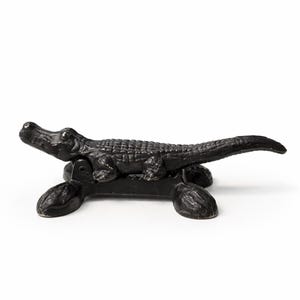 May include: A black alligator-shaped nutcracker. The cast iron nutcracker features a detailed alligator design with a textured body and a hinged jaw for cracking nuts. The alligator is mounted on a base with four feet.