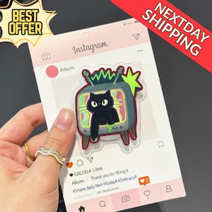 May include: A clear acrylic sticker featuring a black cat inside a retro television set with a colorful screen. The sticker is on a pink Instagram-themed background with the text "BEST OFFER" and "NEXTDAY SHIPPING".
