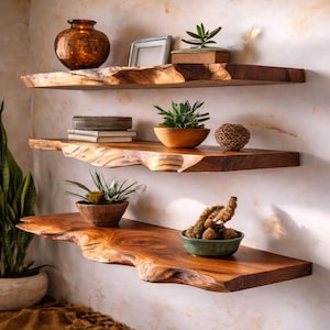 以下が含まれることがあります： 木製のフローティングシェルフ3段。自然なエッジのディテールが施され、テクスチャード加工された壁に取り付けられています。木製のボウルに入った植物、銅の花瓶、織りの球体など、装飾品が飾られています。大きな鉢植えの植物が隅にあります。