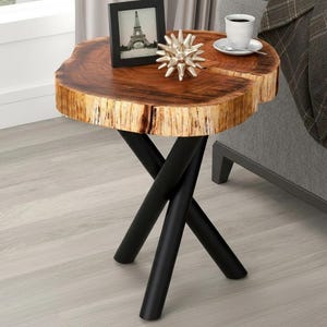 May include: A distinctive side table with a natural wood slab top and black metal legs. The table has a live edge design, displaying the wood's natural grain and colour variations. A small framed photo and decorative object sit on top. The table is approximately 61 cm tall.