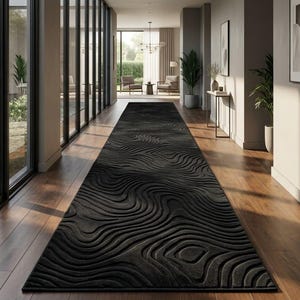 Puede incluir: Una alfombra de pasillo larga y rectangular de color negro con un patrón topográfico tridimensional en relieve de líneas concéntricas y onduladas. La alfombra está colocada en el centro sobre un suelo de madera oscura.