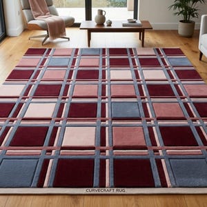 May include: A rectangular area rug with a geometric pattern. The rug features a grid design with squares in shades of burgundy, pink, and gray. The rug is placed on a hardwood floor in a living room setting. The text "CURVECRAFT RUG" is visible.