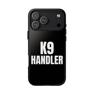 May include: Black phone case with the text "K9 HANDLER" in bold white letters. The case has a glossy finish and features a triple-lens camera system. The design is simple and modern, suitable for dog handlers.