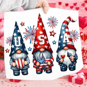 May include: A white print featuring three patriotic gnomes with the letters "USA" on their hats. The gnomes are adorned with red, white, and blue stars and stripes, holding patriotic symbols. Fireworks and stars complete the festive design.