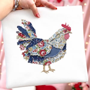 Może przedstawiać: Białe kwadratowe pł&oacute;tno przedstawia aplikację z kogutem z tkaniny. Kogut wykonany jest ze skrawk&oacute;w materiału z kwiatowymi i paisley wzorami w kolorze czerwonym, niebieskim i ż&oacute;łtym. Ma czerwony grzebień i podgardle oraz złote nogi.