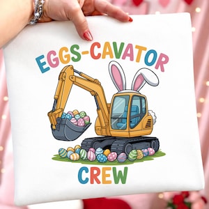 May include: White square pillow with a colorful graphic of a yellow excavator with bunny ears, scooping Easter eggs. The text "EGGS-CAVATOR CREW" is above and below the image in colorful letters.