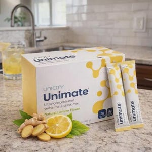 May include: A box of Unicity Unimate yerba mate drink mix with natural lemon flavor. The box is white with yellow accents and the Unimate logo. Two packets of the drink mix are next to the box, along with a lemon and ginger slices.