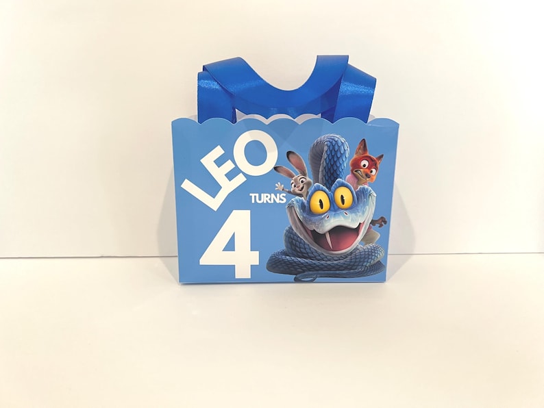 Pode incluir: Uma sacola de presente retangular azul-clara com borda superior recortada e al&ccedil;as de fita azul. A frente apresenta o texto branco LEO TURNS 4 e uma ilustra&ccedil;&atilde;o gr&aacute;fica de uma cobra azul, um coelho e uma raposa de um filme.