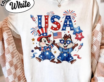 May include: White Comfort Colors sweatshirt with a patriotic design. The graphic features two cartoon chipmunks in denim overalls, holding a flag and wearing sunglasses and a hat. The word "USA" is in red and blue, with fireworks and stars.