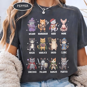 May include: Dark gray t-shirt featuring cartoon cats dressed as fantasy characters, including a wizard, barbarian, and rogue. The text "PEPPER" is in a white oval at the top. Each cat is labeled with its character class.