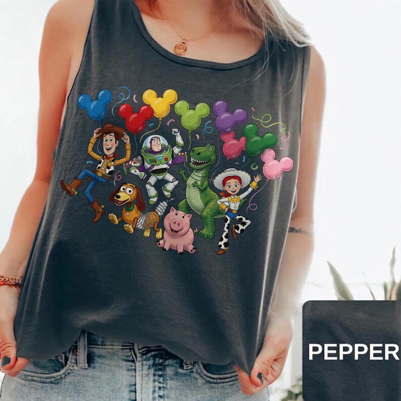 May include: A dark gray sleeveless tank top featuring a graphic print of Toy Story characters including Woody, Buzz Lightyear, Slinky Dog, Hamm, Rex, and Jessie. The characters are surrounded by colorful Mickey Mouse-shaped balloons.