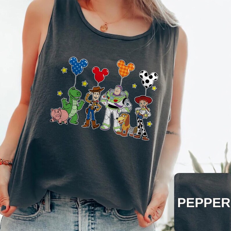 May include: Dark gray tank top featuring a colorful graphic of Toy Story characters holding Mickey Mouse-shaped balloons. The characters include Woody, Buzz Lightyear, and Jessie. The word "PEPPER" is printed on a black rectangle.