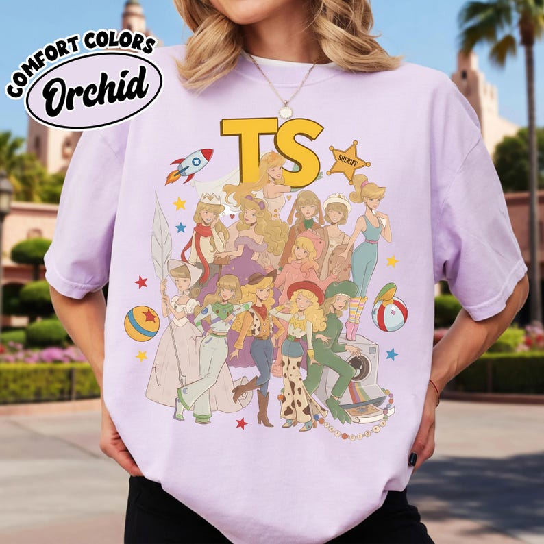 May include: A light purple short-sleeve t-shirt featuring a graphic print of various animated characters in diverse outfits, including a rocket, a sheriff badge, and balls. The text "COMFORT COLORS", "Orchid", and "TS" are printed on the shirt.