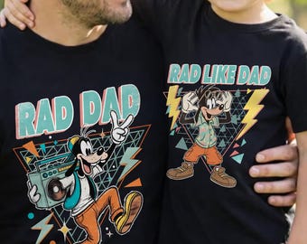 May include: Black t-shirts with matching graphics. One shirt says "RAD DAD" with a cartoon dog holding a boombox. The other says "RAD LIKE DAD" with a cartoon dog wearing sunglasses. Both shirts have a retro 80s design.