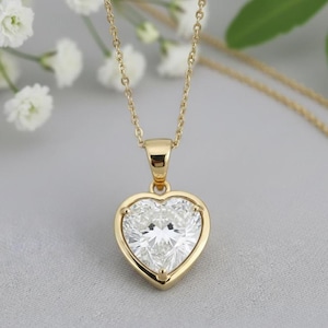 Peut inclure: Un collier doré avec un pendentif en forme de cœur. Le pendentif présente une grosse pierre précieuse claire taillée en cœur, sertie dans une lunette dorée. La chaîne est délicate et dorée.