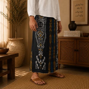 May include: A sarong featuring a dark navy blue base with intricate vertical patterns in shades of mustard yellow, white, and light blue. The fabric displays a repeating ikat-style design with geometric motifs and scrollwork, worn with brown sandals.