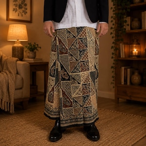 May include: A sarong featuring a geometric patchwork pattern in shades of brown, black, and cream. The fabric displays intricate batik-style motifs within triangular segments, finished with a dark border at the hem, worn with a white shirt and blazer.